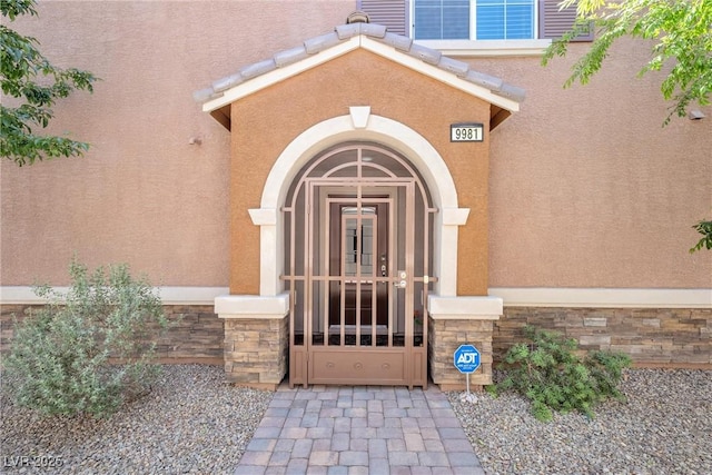 view of exterior entry featuring a gate, stucco siding, and stone siding