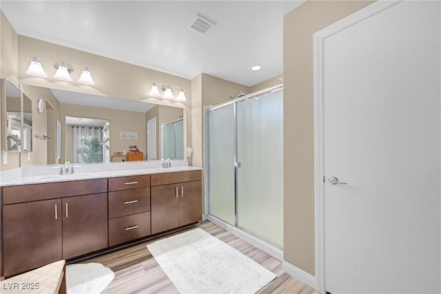 full bathroom with visible vents, double vanity, wood finished floors, a shower stall, and a sink