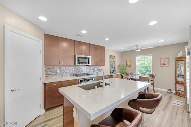 kitchen with a sink, appliances with stainless steel finishes, decorative backsplash, and light wood-style flooring