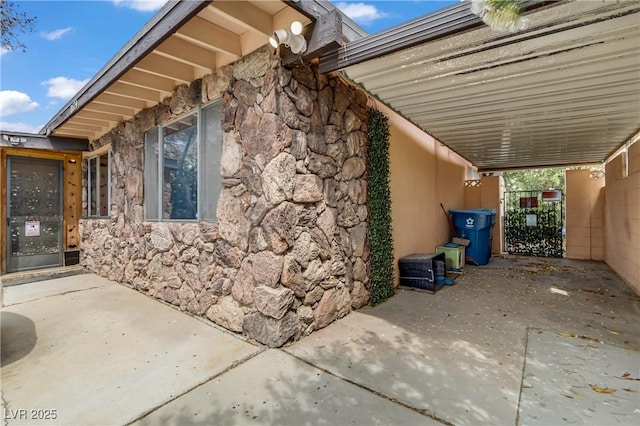 view of property exterior with a gate, stucco siding, stone siding, and a carport