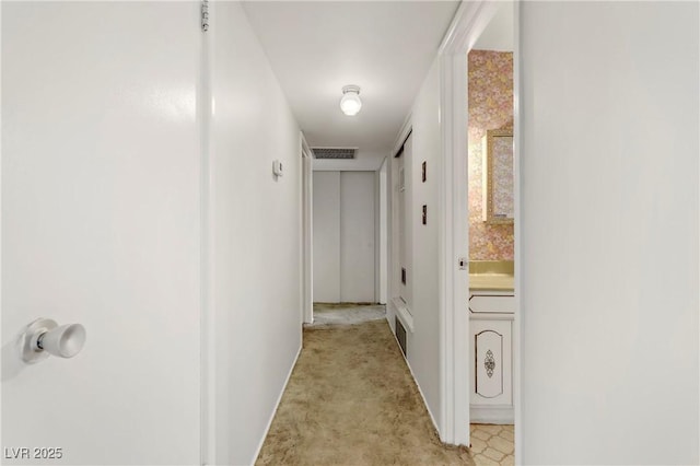 hallway featuring baseboards, visible vents, and light carpet