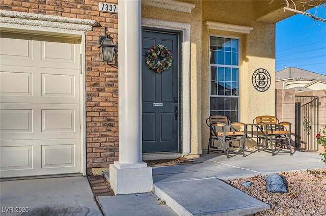 entrance to property with brick siding, a garage, and stucco siding