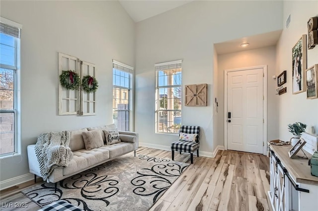 living area with visible vents, light wood-style flooring, a towering ceiling, and baseboards
