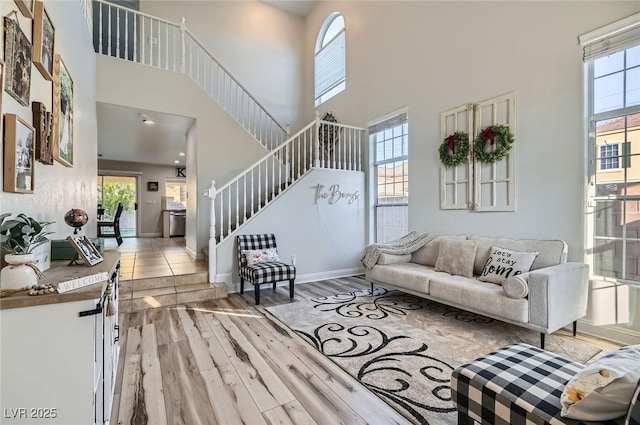 living room featuring plenty of natural light, a high ceiling, light wood-type flooring, and stairs