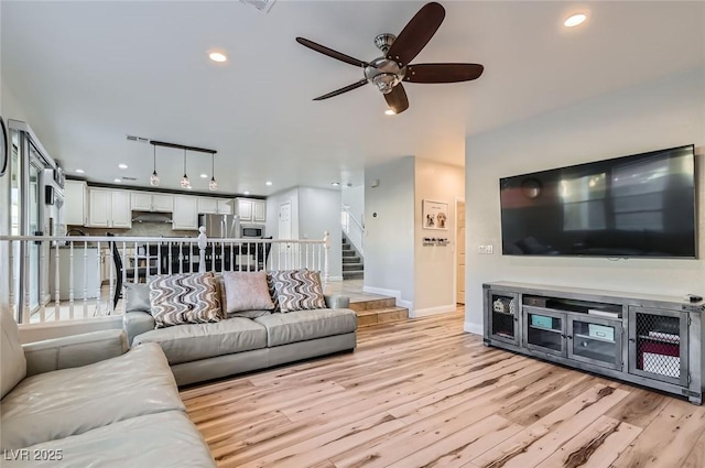 living room with ceiling fan, light wood-style floors, recessed lighting, baseboards, and stairway