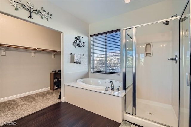 full bath featuring a garden tub, a shower stall, wood finished floors, baseboards, and a spacious closet
