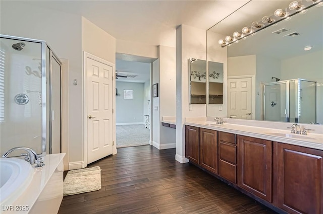 full bath with double vanity, a shower stall, a sink, and wood finished floors