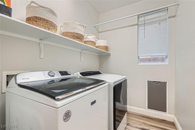 clothes washing area with laundry area, baseboards, washing machine and dryer, and light wood-type flooring