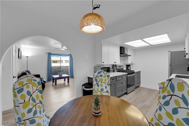 dining space featuring light wood-type flooring, arched walkways, and baseboards
