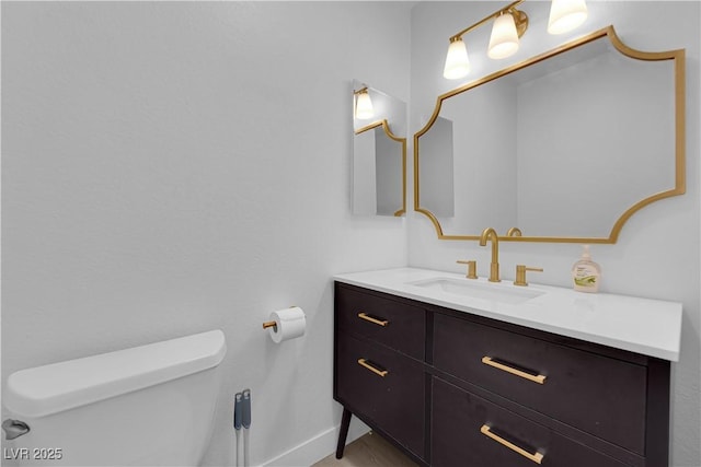 half bathroom featuring toilet, baseboards, and vanity