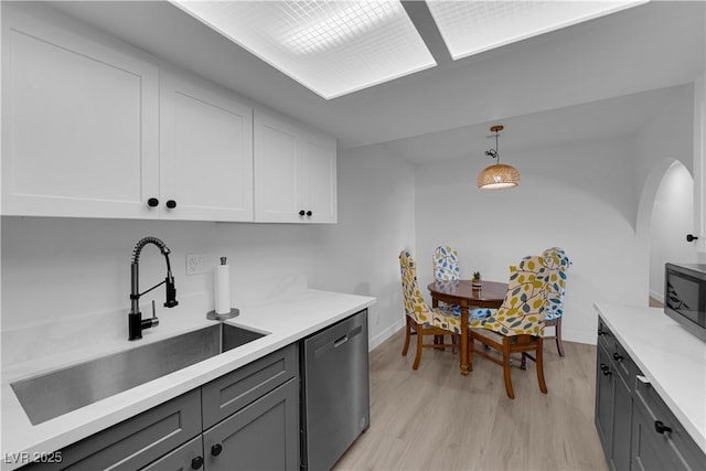 kitchen featuring light wood-type flooring, dishwasher, a sink, light countertops, and white cabinetry