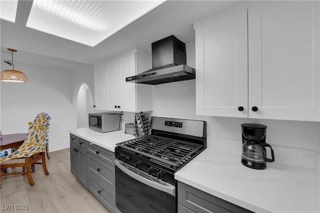 kitchen with wall chimney range hood, arched walkways, gray cabinetry, and stainless steel appliances