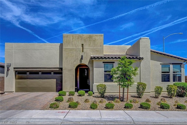 southwest-style home with a tiled roof, a garage, driveway, and stucco siding