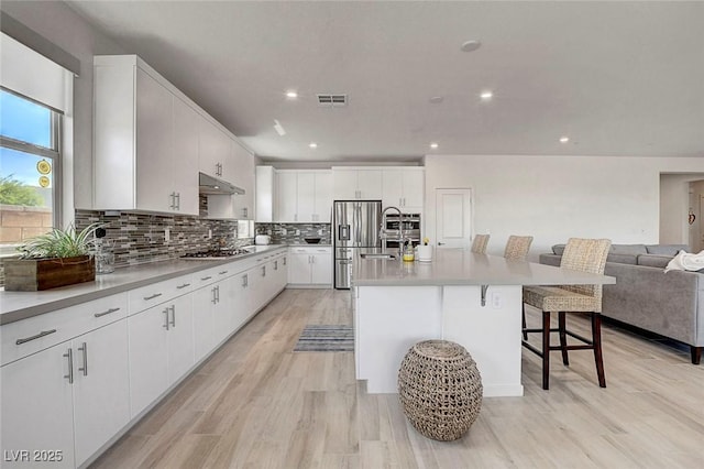 kitchen featuring backsplash, appliances with stainless steel finishes, open floor plan, light wood-style floors, and a breakfast bar