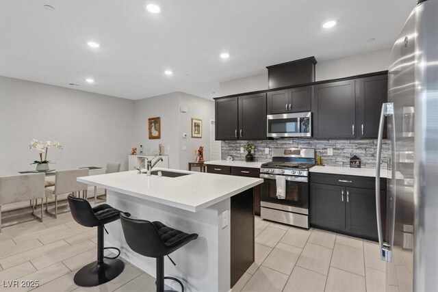 143 Aqua Commons Ln, Henderson, NV 89015 - kitchen with stainless steel appliances, a sink, backsplash, light countertops, and a kitchen island with sink