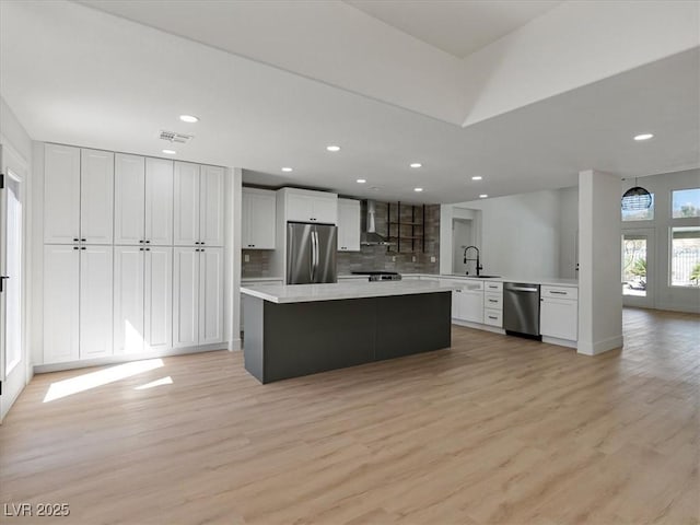kitchen with wall chimney range hood, light countertops, stainless steel appliances, decorative backsplash, and visible vents