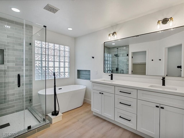 bathroom featuring a sink, a stall shower, wood finished floors, and visible vents