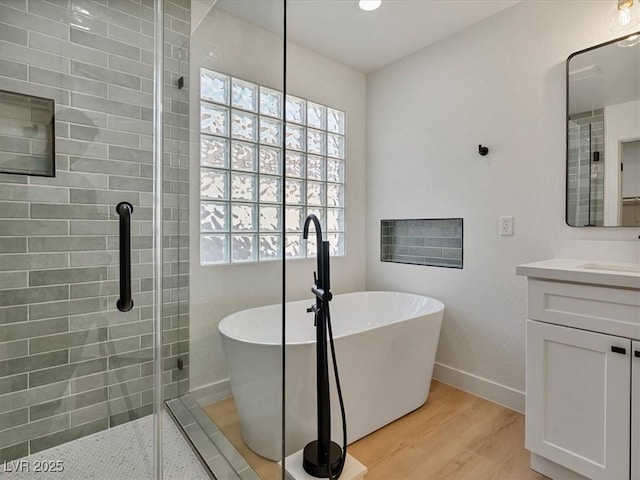 bathroom with vanity, a freestanding tub, baseboards, wood finished floors, and tiled shower