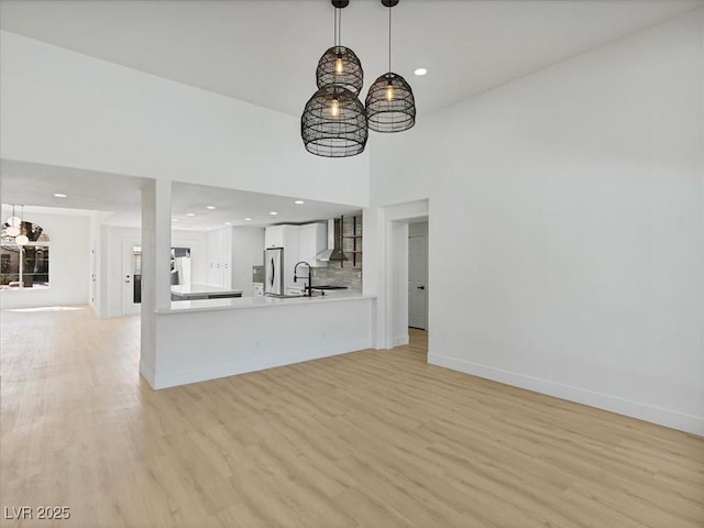 unfurnished living room with light wood-type flooring, recessed lighting, baseboards, and a notable chandelier
