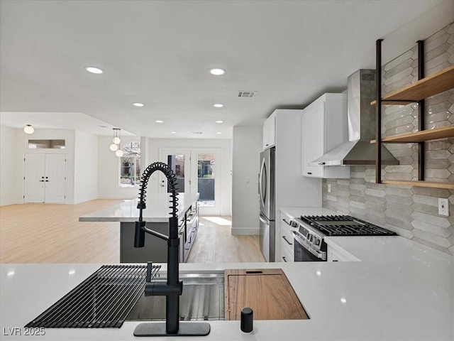 kitchen with visible vents, appliances with stainless steel finishes, white cabinets, light wood-style floors, and wall chimney exhaust hood