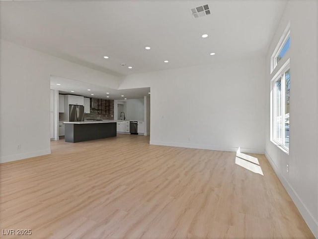 unfurnished living room with recessed lighting, baseboards, a sink, and light wood-style floors