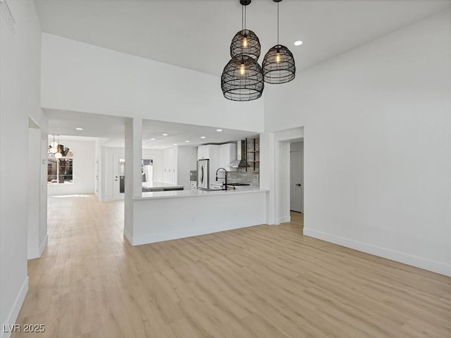 unfurnished living room featuring light wood-type flooring, baseboards, a notable chandelier, a high ceiling, and recessed lighting