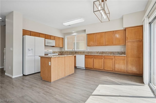 kitchen with white appliances, light stone countertops, a kitchen island, and light wood-style floors