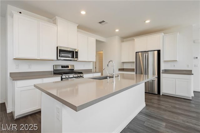 kitchen featuring appliances with stainless steel finishes, a sink, an island with sink, white cabinetry, and visible vents