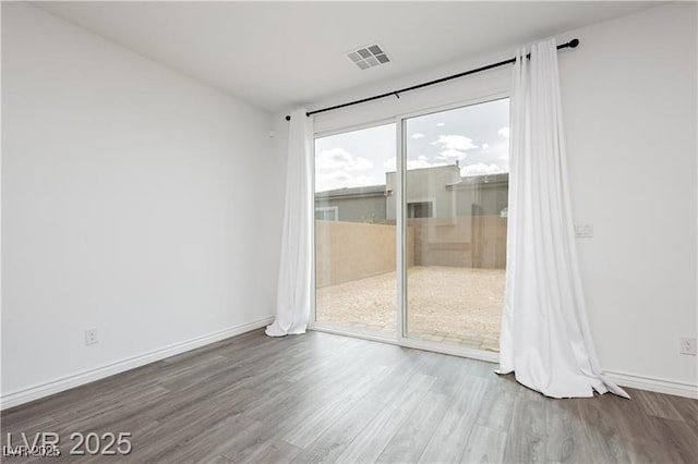 spare room featuring baseboards, wood finished floors, and visible vents