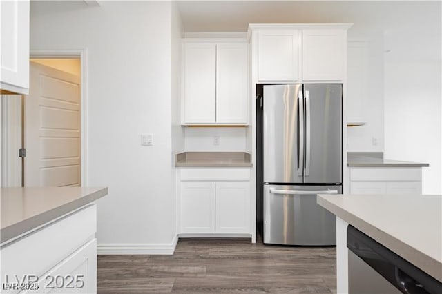 kitchen with white cabinets, appliances with stainless steel finishes, light countertops, baseboards, and wood finished floors
