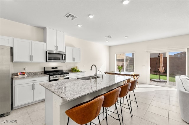 kitchen with a sink, appliances with stainless steel finishes, light stone countertops, and visible vents