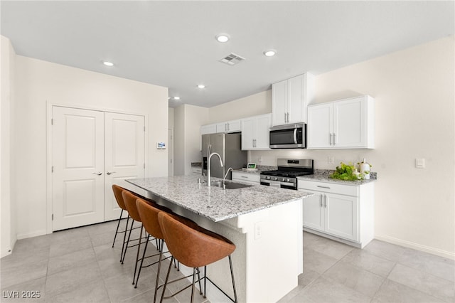 kitchen with appliances with stainless steel finishes, a sink, a kitchen breakfast bar, an island with sink, and visible vents