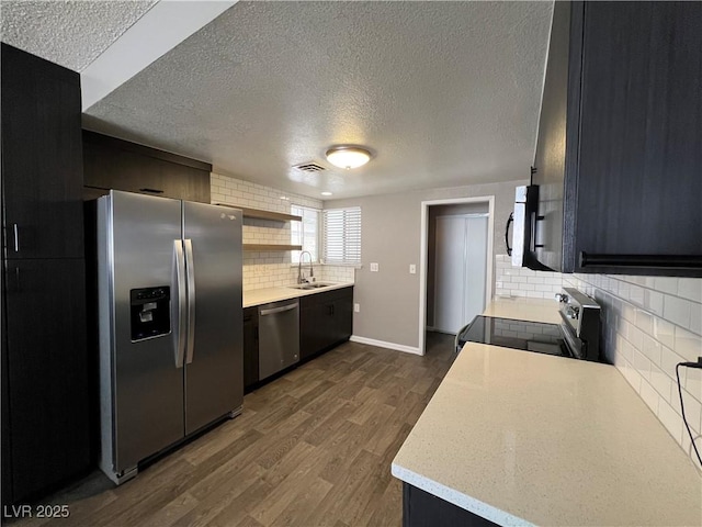 kitchen with appliances with stainless steel finishes, a sink, a textured ceiling, dark wood finished floors, and backsplash