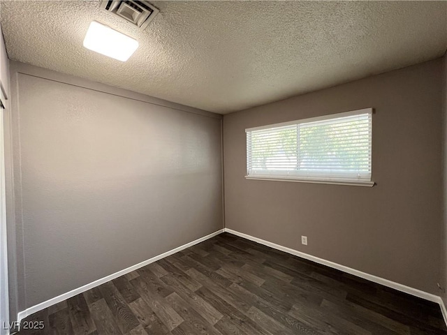 unfurnished room featuring baseboards, dark wood finished floors, a textured ceiling, and visible vents
