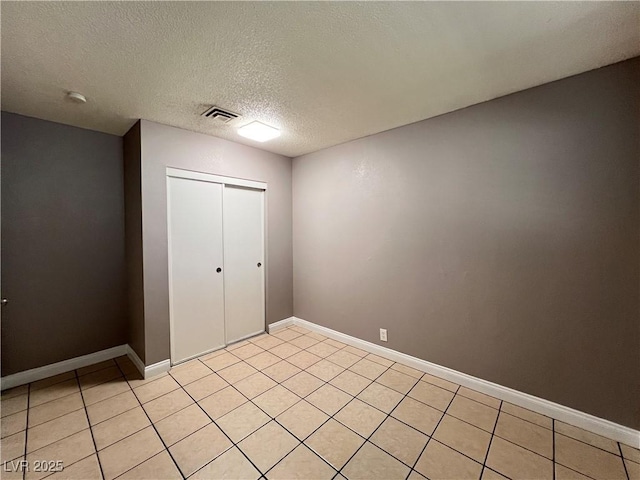 unfurnished bedroom featuring light tile patterned flooring, a textured ceiling, baseboards, visible vents, and a closet