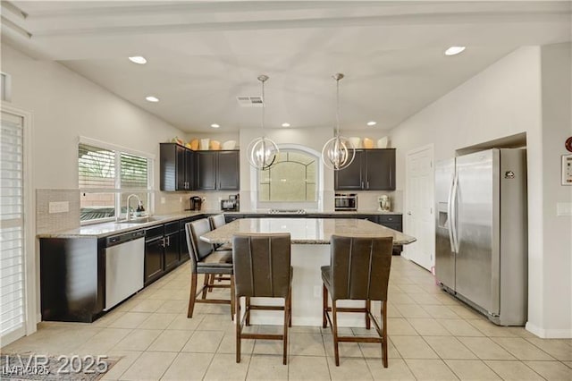 kitchen with a breakfast bar area, appliances with stainless steel finishes, a center island, a sink, and a notable chandelier