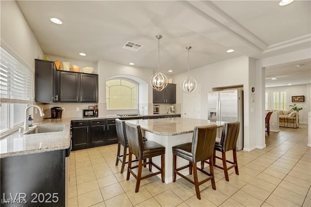 kitchen featuring light stone countertops, a breakfast bar, a sink, light tile patterned floors, and visible vents