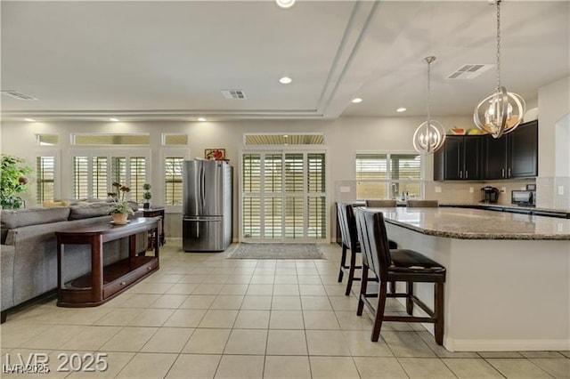kitchen with visible vents, freestanding refrigerator, light tile patterned flooring, a chandelier, and stone counters