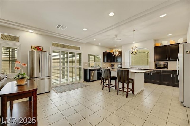 kitchen with appliances with stainless steel finishes, light countertops, a kitchen breakfast bar, a kitchen island, and visible vents