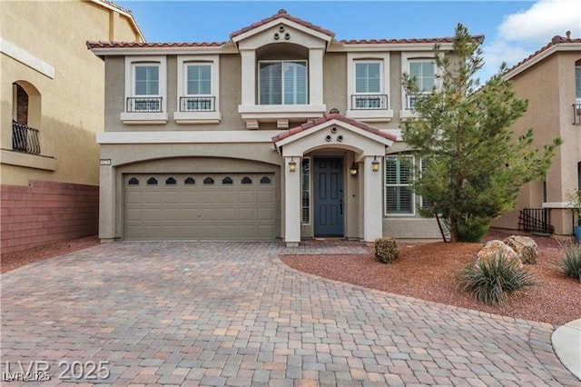 mediterranean / spanish-style home with an attached garage, decorative driveway, stucco siding, and a tiled roof