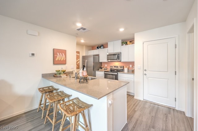 kitchen with a breakfast bar area, visible vents, appliances with stainless steel finishes, light wood finished floors, and white cabinetry