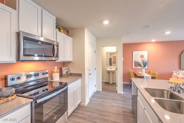 kitchen featuring a sink, light stone counters, white cabinets, stainless steel appliances, and light wood-style flooring