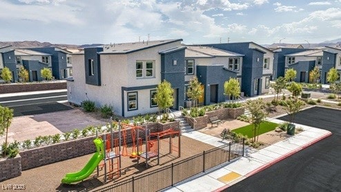 rear view of property featuring stucco siding, a playground, fence, and a residential view