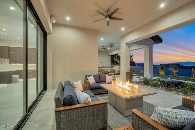 patio terrace at dusk with an outdoor living space with a fire pit, ceiling fan, and exterior kitchen