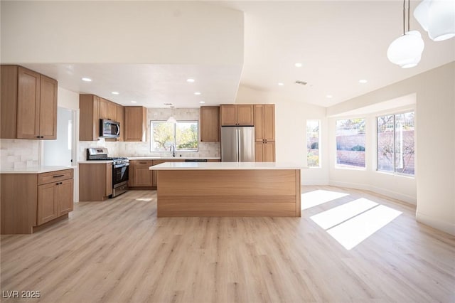 kitchen featuring appliances with stainless steel finishes, light wood-style floors, light countertops, a center island, and backsplash