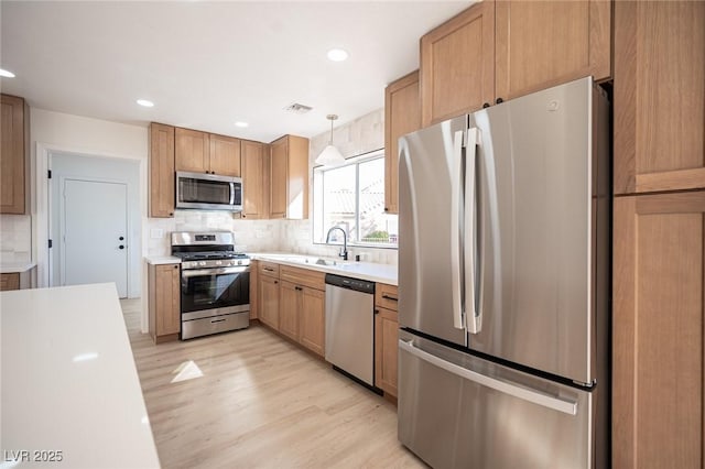 kitchen featuring decorative backsplash, light wood finished floors, appliances with stainless steel finishes, and light countertops