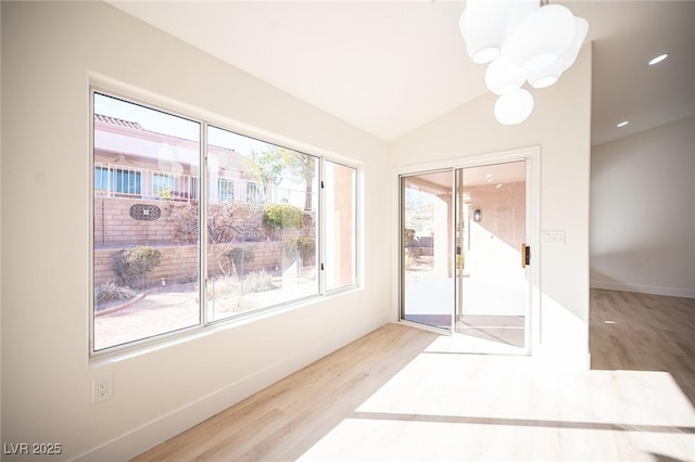 interior space with baseboards, a chandelier, wood finished floors, and lofted ceiling