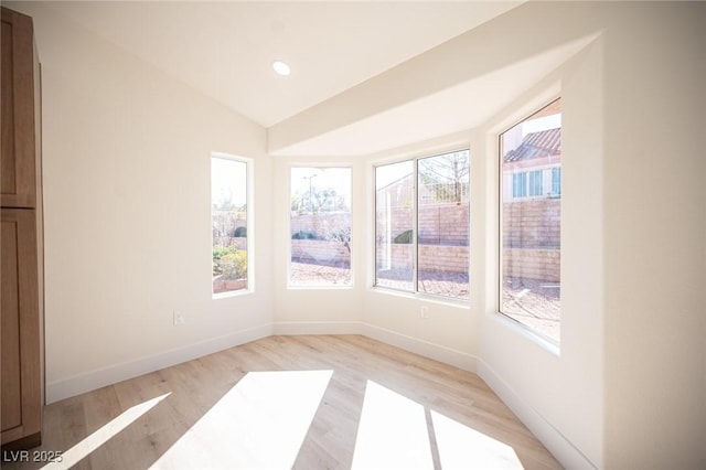 empty room with baseboards, vaulted ceiling, a wealth of natural light, and light wood-type flooring