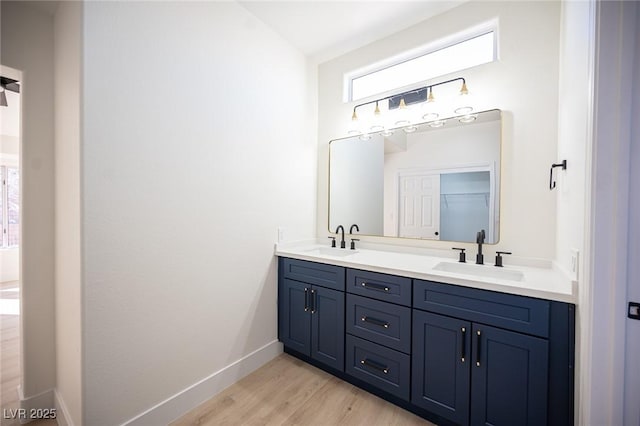 bathroom with double vanity, a sink, baseboards, and wood finished floors
