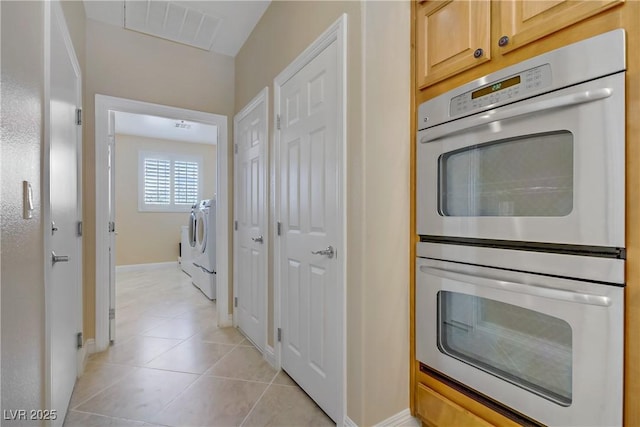 kitchen featuring stainless steel double oven, visible vents, light brown cabinetry, light tile patterned floors, and baseboards